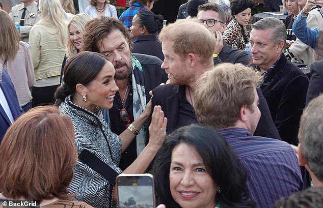 Meghan is spotted affectionately holding Harry while another guest seems to be getting her photo taken with the couple in the background