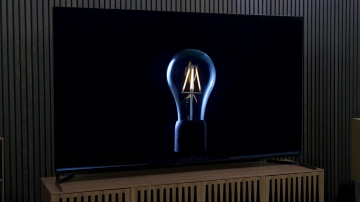 Die Glühfäden einer Glühbirne leuchten schwach und beleuchten den Umriss der Glühbirne auf einem Sony X95L Mini-LED-Fernseher. 