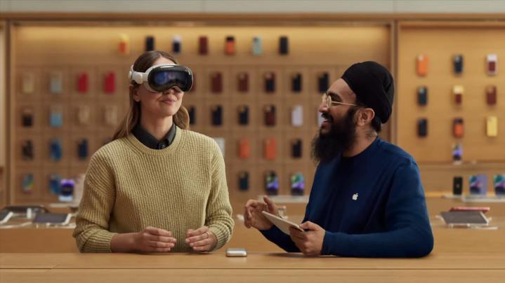 Eine Person probiert in einem Apple Store ein Apple Vision Pro Mixed-Reality-Headset an, an ihrer Seite ein Apple-Mitarbeiter.