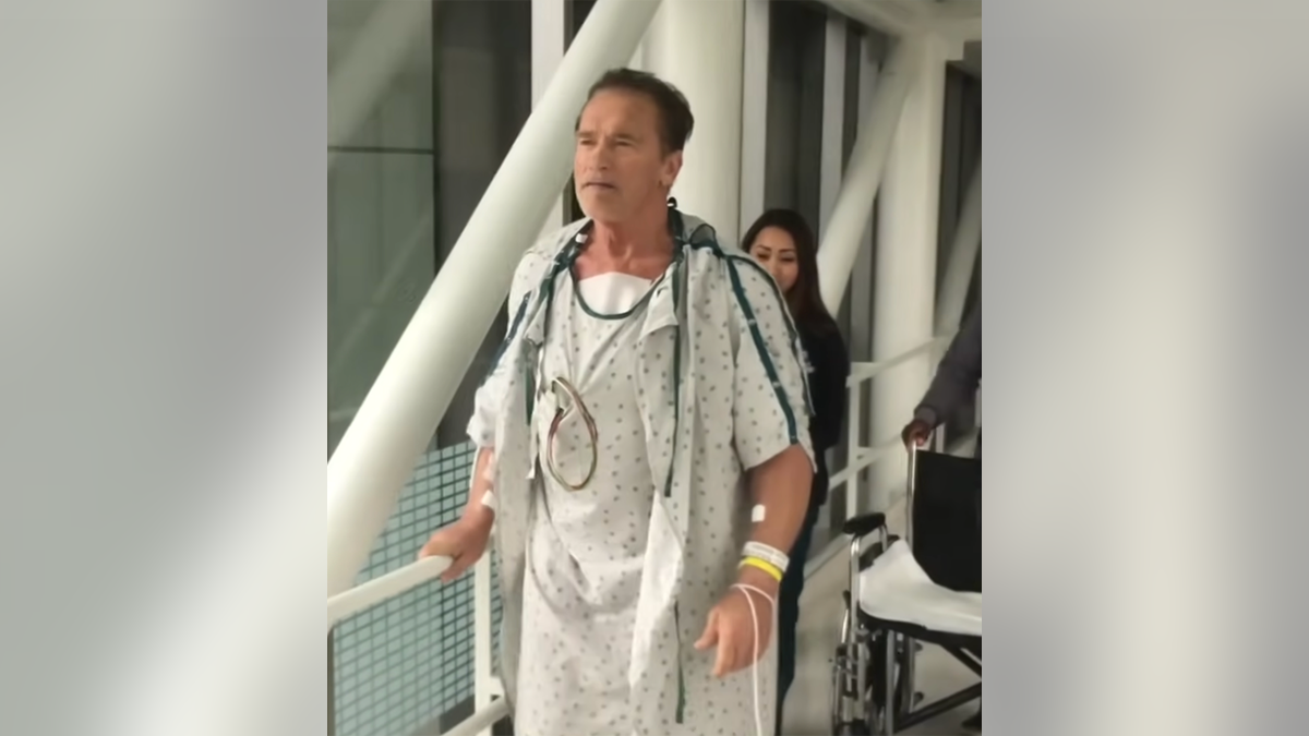 Arnold Schwarzenegger geht im Kittel durch die Flure des Krankenhauses
