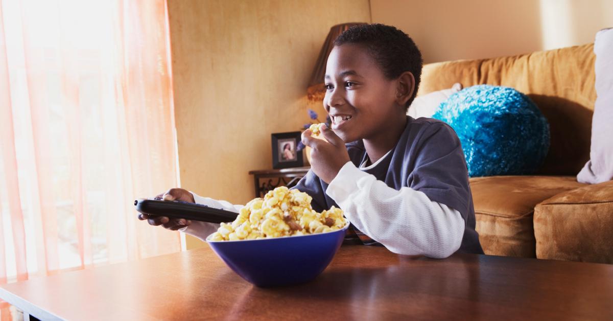 Ein Junge isst Popcorn und schaut sich einen Film in seinem Wohnzimmer an.
