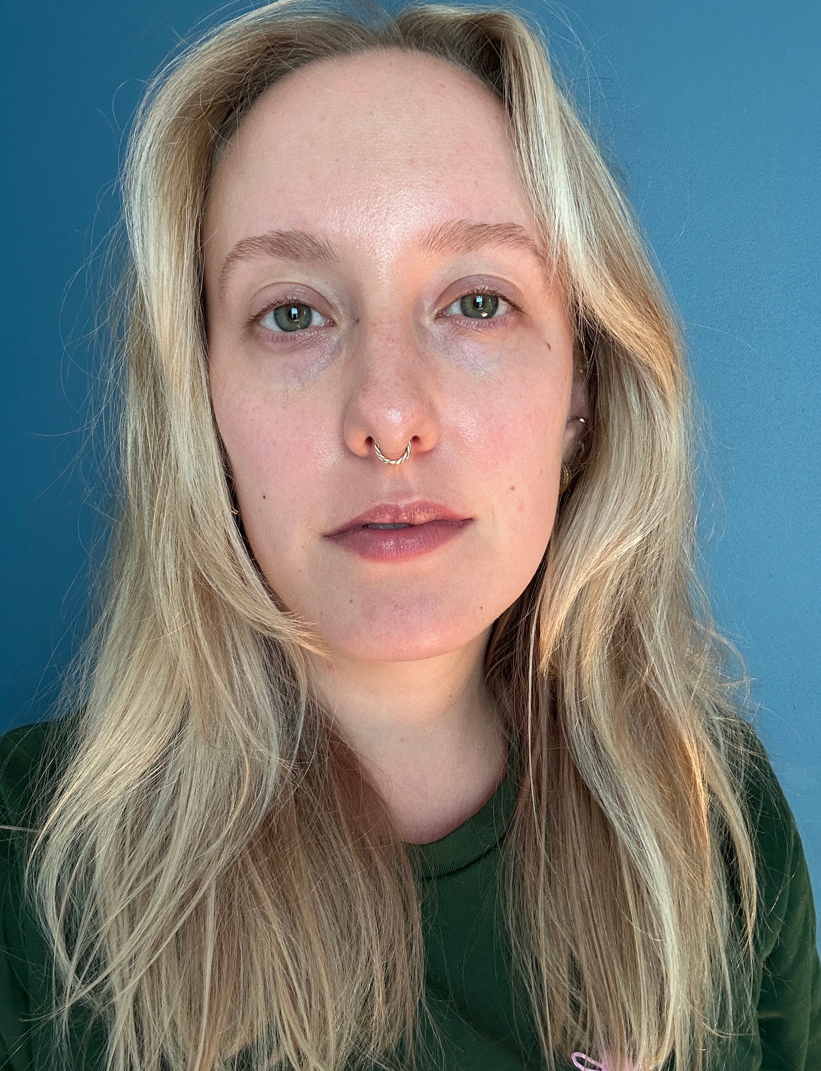 Ein Vorher-Foto einer Frau ohne Make-up, die vor einer blauen Wand steht