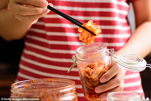 Das Bild zeigt jemanden, der mit Stäbchen Kimchi aus einem Glas holt.  Kombucha, Kimchi und Sauerkraut enthalten von Natur aus probiotische Bakterien, die bei Ihrem Kater helfen können
