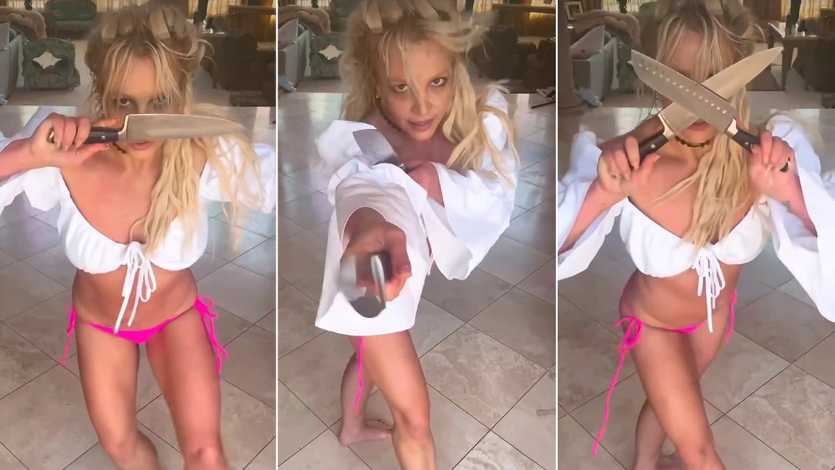 Britney Spears trägt einen rosa Bikini und ein weißes Oberteil und trägt Requisitenmesser