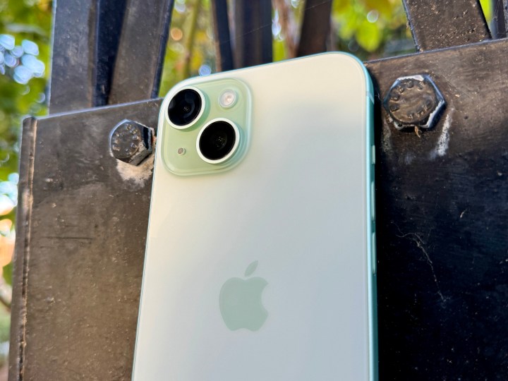A green iPhone 15 showing the camera and matte glass back.