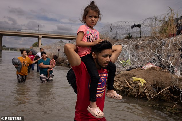 Alejandro aus Honduras trägt seine vierjährige Tochter Soy, als sie am Freitag in Eagle Pass, Texas, an einem Drahtzaun vorbeigehen, während sie nach einem Einreisepunkt in die USA suchen