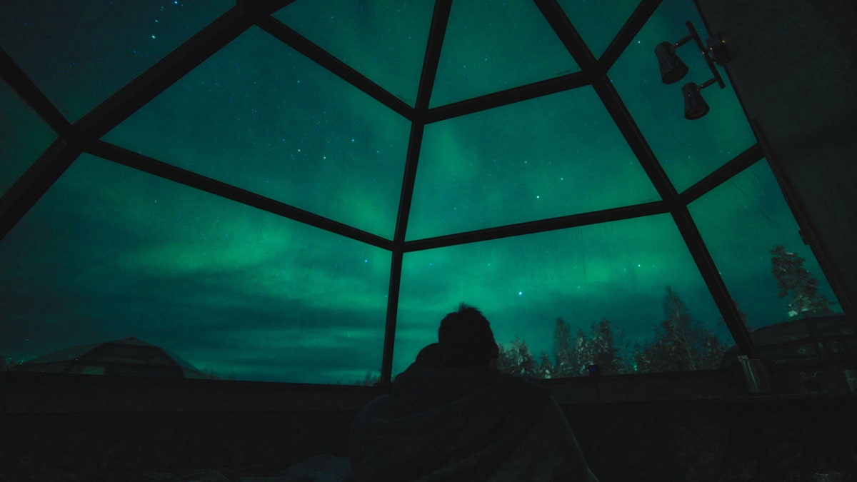 Ein Paar genießt den Blick auf Aurora Borealis und die Sterne in einem Glas-Iglu in Lappland, Rovaniemi, Finnland