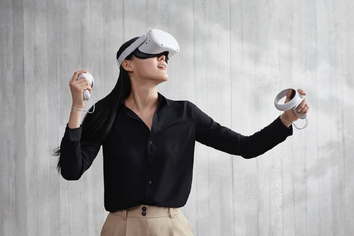 Eine Person, die ein Oculus Quest 2 VR-Headset trägt und verwendet, vor einem grauen Hintergrund.