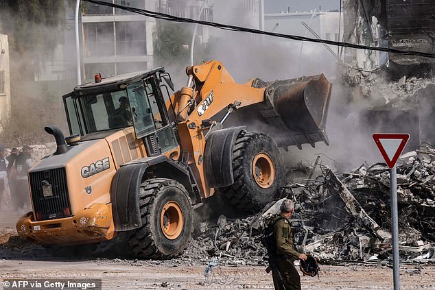 A member of the Israeli security forces looks on as a bulldozer clears rubble in front of a police station in Sderot after it was damaged during battles to dislodge Hamas terrorists who were stationed inside, on October 8