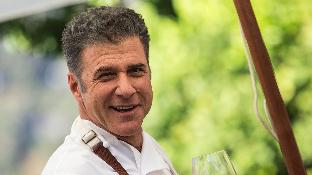 Michael Chiarello hält lächelnd ein Weinglas in einem Weinberg