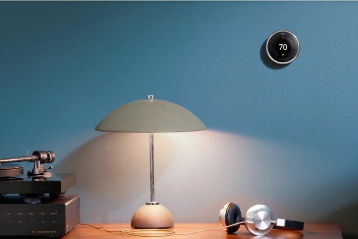 Der Google Nest Learning Thermostat ist an einer Bürowand über einem Schreibtisch und einer Lampe montiert.