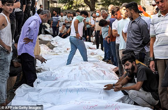 EDITORS NOTE: Graphic content / People stand by the bodies of victims of Israeli air strikes outside the morgue of al-Shifa hospital in Gaza City on October 12, 2023 as raging battles between Israel and the Hamas movement continue for the sixth consecutive day. Thousands of people, both Israeli and Palestinians have died since October 7, 2023, after Palestinian Hamas militants based in the Gaza Strip, entered southern Israel in a surprise attack leading Israel to declare war on Hamas in Gaza on October 8. (Photo by MOHAMMED ABED / AFP) (Photo by MOHAMMED ABED/AFP via Getty Images)