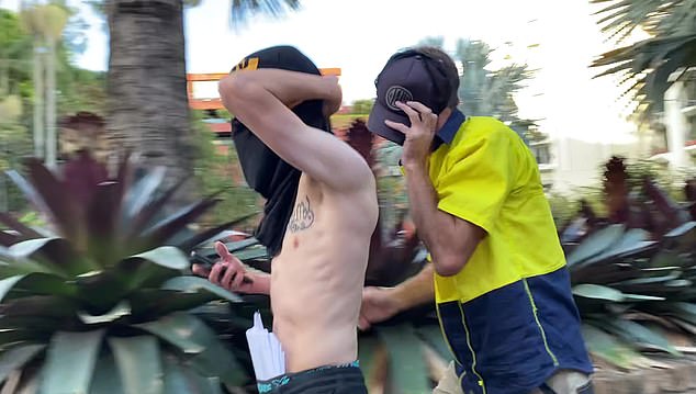 Ein Mann bedeckte sein Gesicht mit einem T-Shirt, während ein anderer, der ein Warnhemd trug, sein Gesicht mit einer Mütze schützte