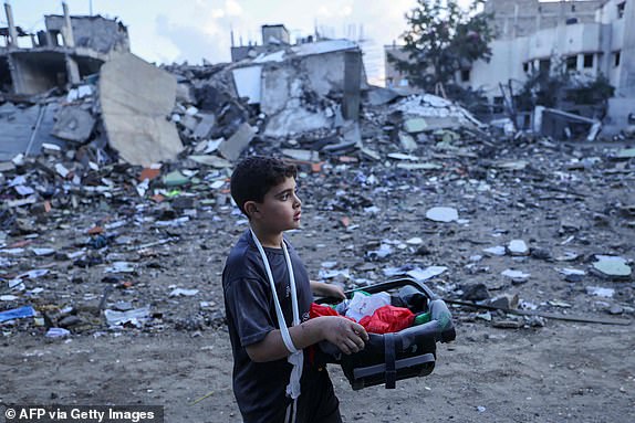 TOPSHOT - A Palestinian boy carries salvageable items amid the rubble of buildings destroyed during Israeli airstrikes in the Rafah refugee camp in the southern of Gaza Strip, on October 16, 2023. Israel declared war on the Islamist group Hamas on October 8, a day after waves of its fighters broke through the heavily fortified border and killed more than 1,400 people, most of them civilians. The relentless Israeli bombings since have flattened neighbourhoods and left at least 2,670 people dead in the Gaza Strip, the majority ordinary Palestinians. (Photo by MOHAMMED ABED / AFP) (Photo by MOHAMMED ABED/AFP via Getty Images)