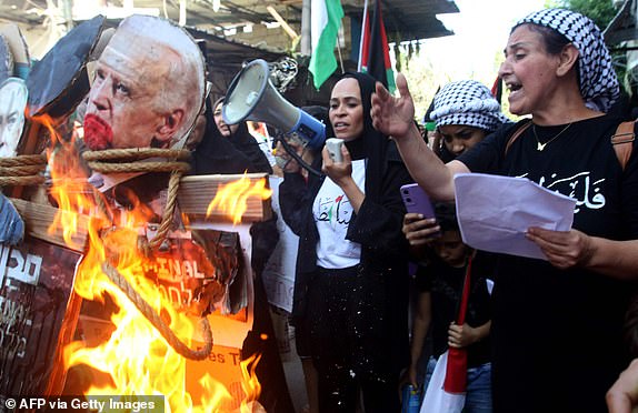 TOPSHOT - A woman speaks as an image of US President Joe Biden is burnt during a protest in the Ain al-Hilweh Palestinian refugee camp near the southern Lebanese port city of Sidon on October 18, 2023, as the US President visited neighbouring Israel, and a day after a strike on the Ahli Arab hospital in Gaza City that killed hundreds. US President Joe Biden on a solidarity visit to Israel on October 18, 2023, backed the ally's account that Palestinian militants caused a devastating hospital strike in Gaza, adding Hamas had brought "only suffering." (Photo by Mahmoud ZAYYAT / AFP) (Photo by MAHMOUD ZAYYAT/AFP via Getty Images)