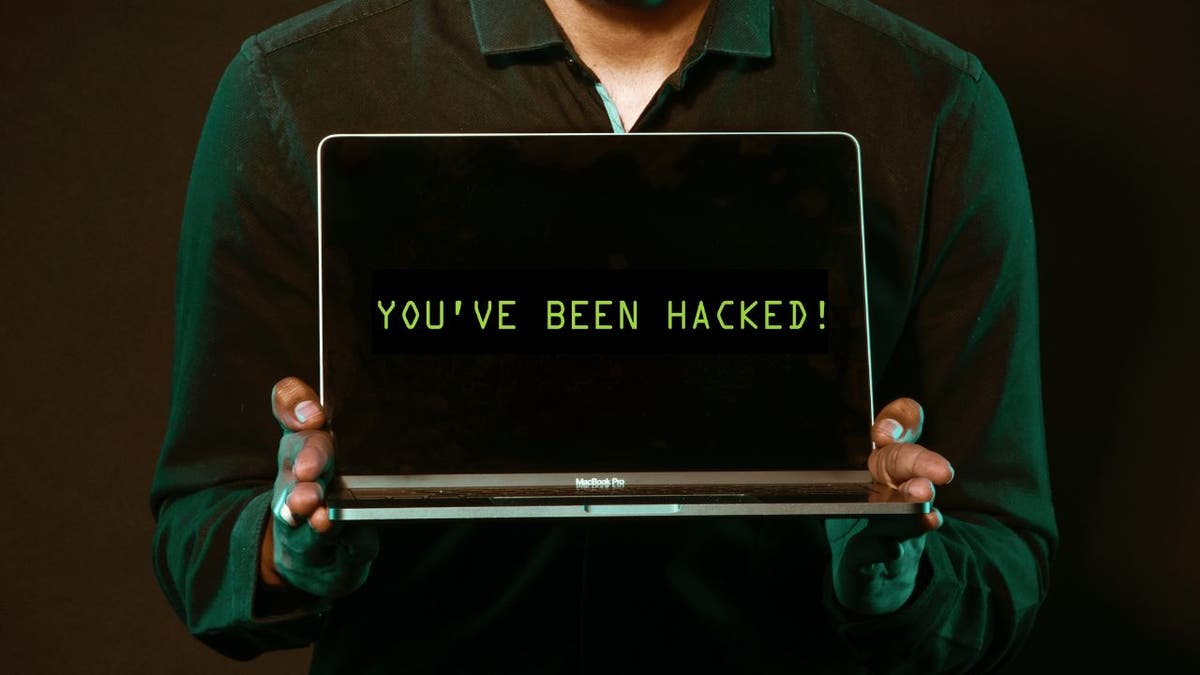 Person hält einen Laptop mit den Worten hoch "Du wurdest gehackt!" auf dem Bildschirm.