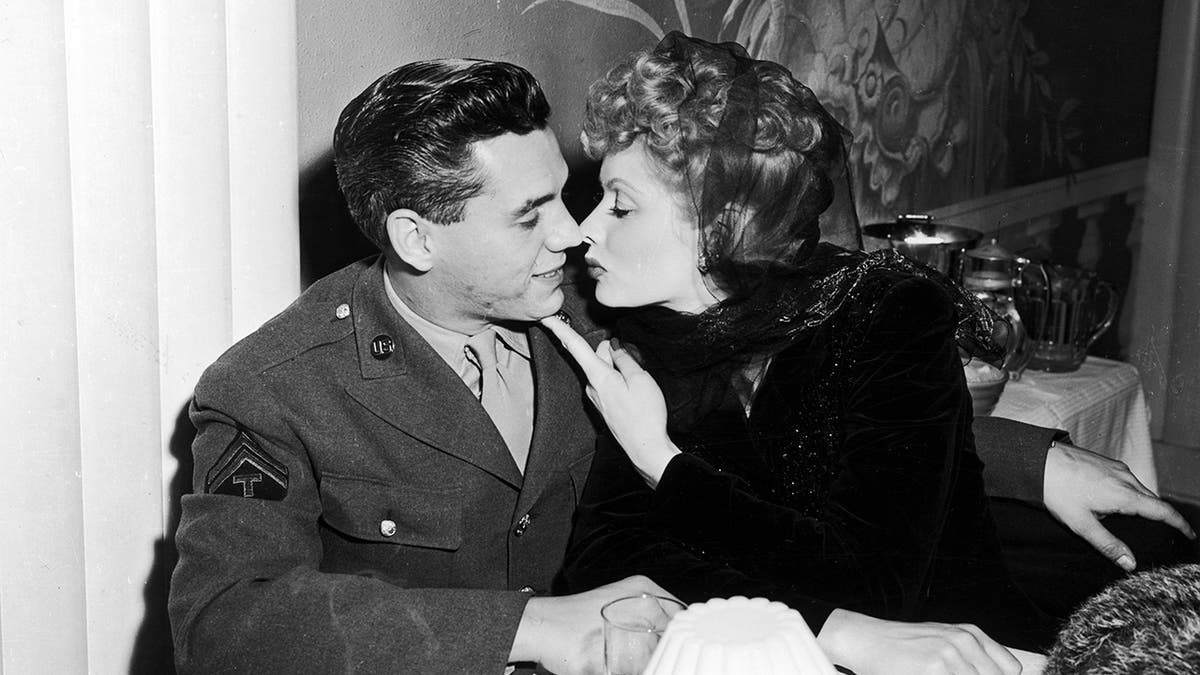 Lucille Ball trägt ein schwarzes Kleid und beugt sich zu einem Kuss von Desi Arnaz in einem Militäranzug vor