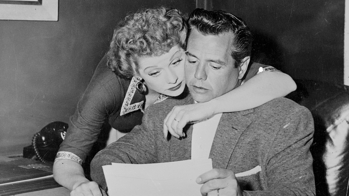 Lucille Ball umarmt Desi Arnaz von hinten, während er einen Brief liest