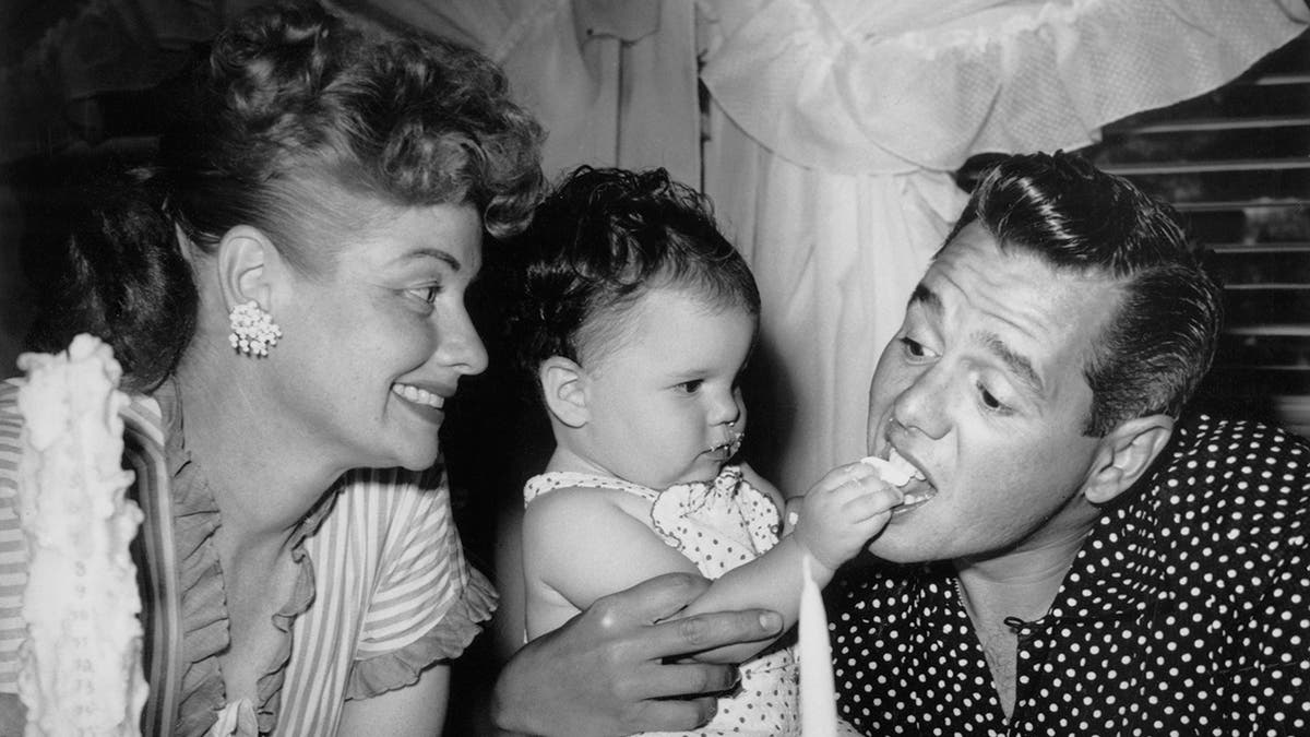 Lucille Ball lächelt, während ihre Tochter Lucie Arnaz ihrem Vater Desi Arnaz ein Stück Kuchen füttert