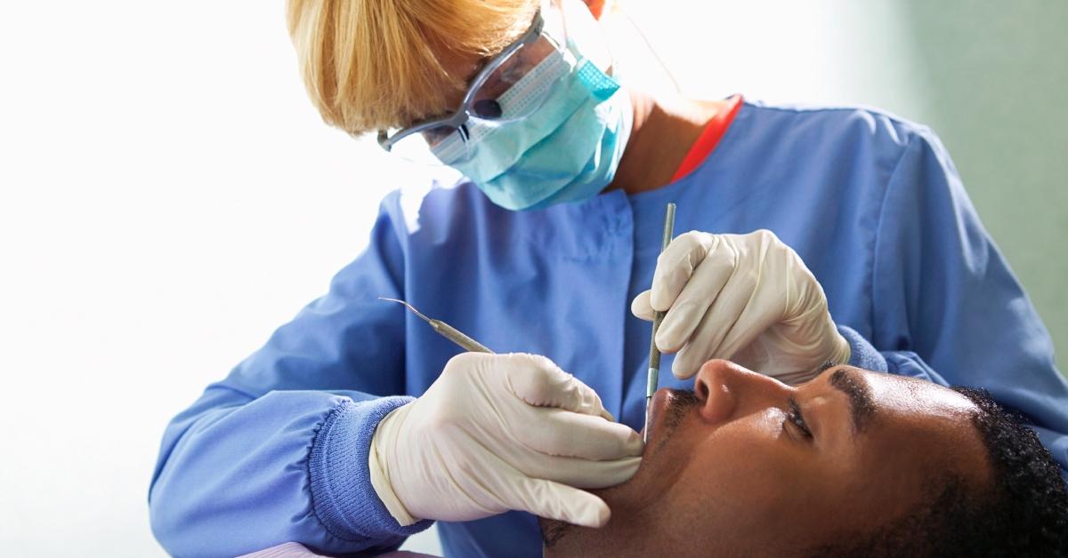 Eine Dentalhygienikerin reinigt die Zähne eines Patienten