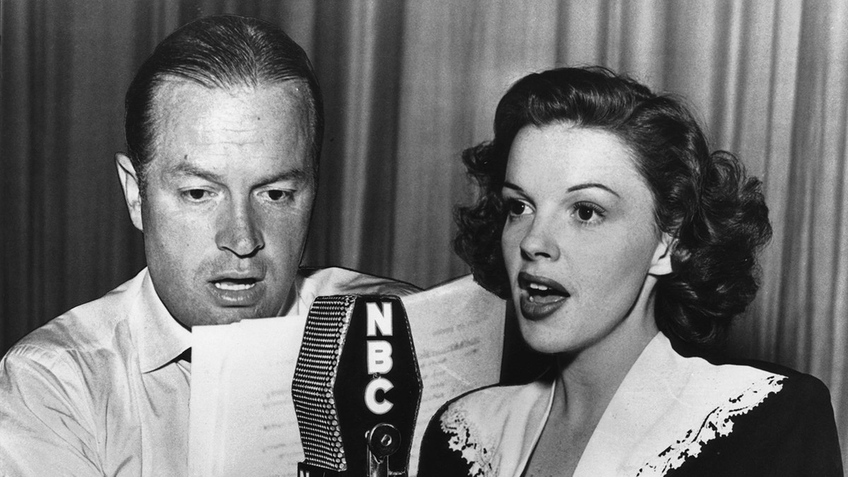 Judy Garland singt vor einem NBC-Mikrofon, während Bob Hope aus einer Zeitung vorliest