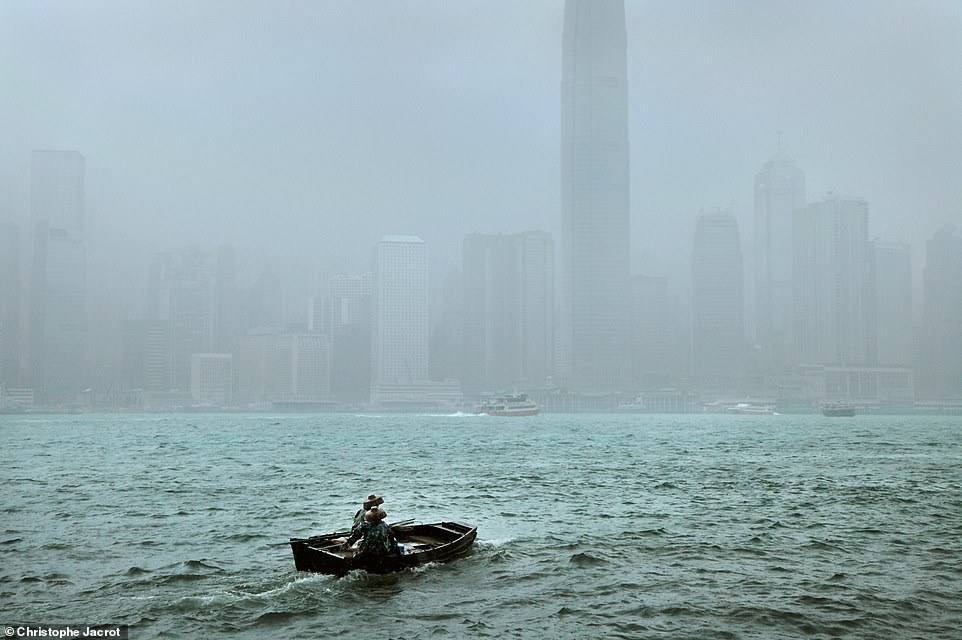 Dieses Bild zeigt ein Boot, das durch unruhige Gewässer in Hongkong fährt.  Jacrot schreibt, dass es „herausfordernd“ sei, gute Aussichtspunkte für die Stadtaufnahmen bei Regenwetter zu finden, er es aber liebe, „mit den Auswirkungen des Regens zu arbeiten“.