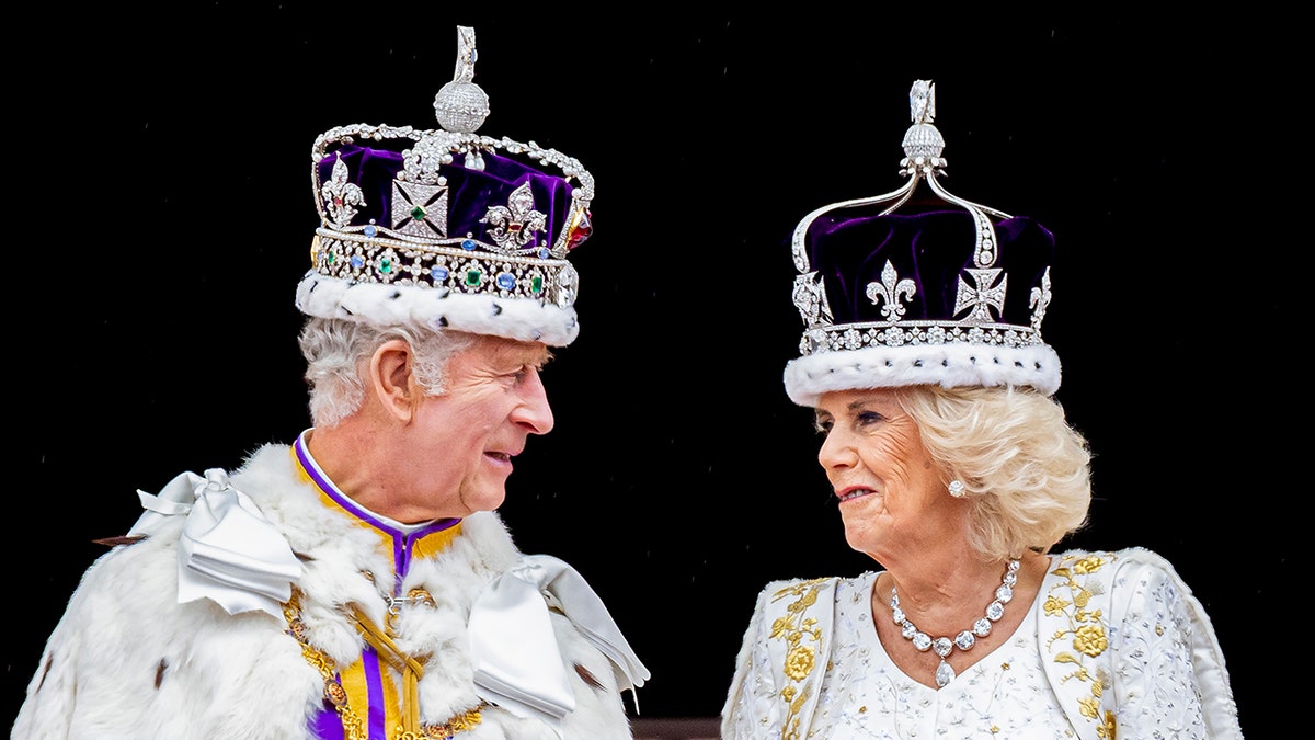 Eine Nahaufnahme von König Charles und Königin Camilla, die einander anschauen, während sie ihre Roben und Kronen tragen