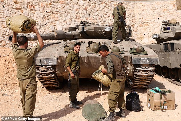 Israeli soldiers make preparations in front of Merkava tanks as they man a position at an undisclosed location on the border with Lebanon