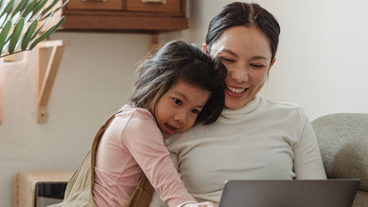 Tochter umarmt Mutter, während sie auf den Laptop schauen