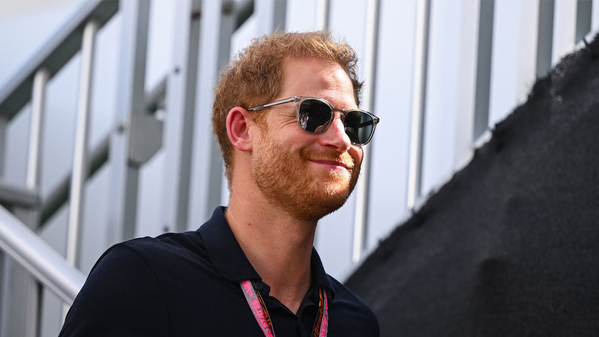 Prinz Harry lächelt, während er beim F1-Rennen eine Sonnenbrille trägt