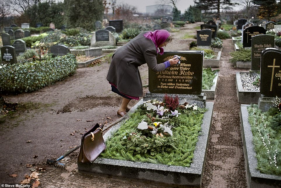 Der zarte Moment, in dem eine Frau 1989 in Ostdeutschland – dem Jahr des Falls der Berliner Mauer – den Grabstein des Grabes ihres verstorbenen Mannes reinigt