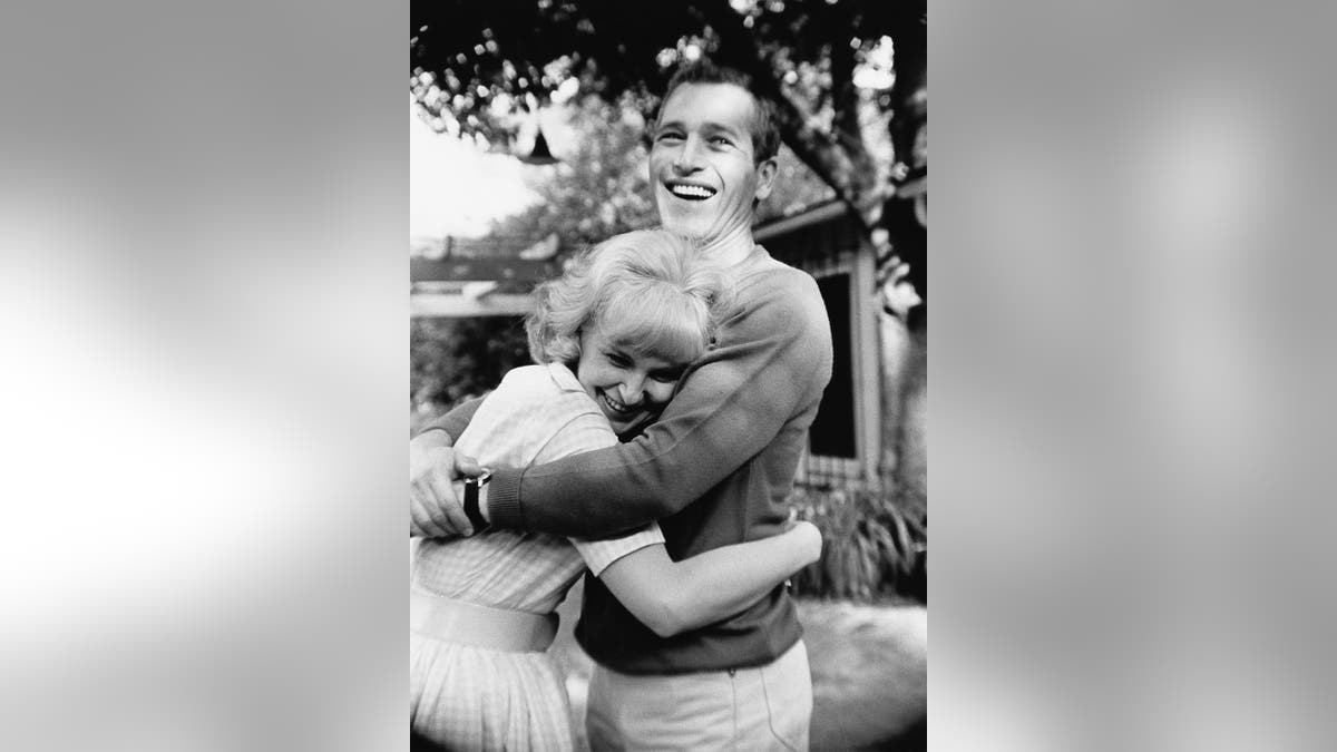Ein lächelnder Paul Newman umarmt draußen eine lachende Joanne Woodward