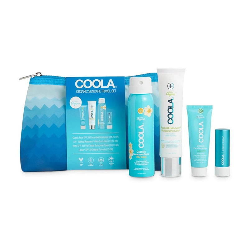 Coola Suncare Reiseset: Eine blau-weiße Aerosol-Sonnenschutzspraydose, eine weiße Tube, eine hellblaue Tube und ein Lippenbalsam mit blauer Kappe sowie eine passende Tragetasche auf weißem Hintergrund