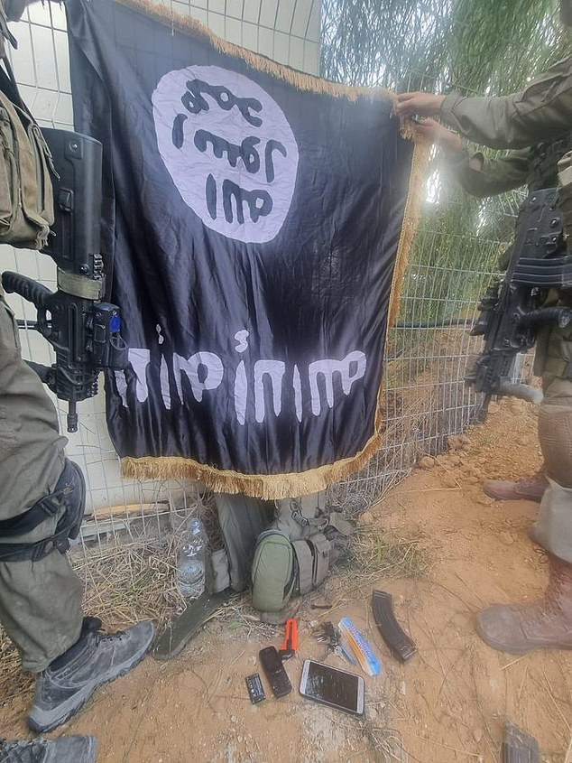 Israeli soldiers are seen holding an ISIS flag allegedly left behind by Hamas gunmen in Israel