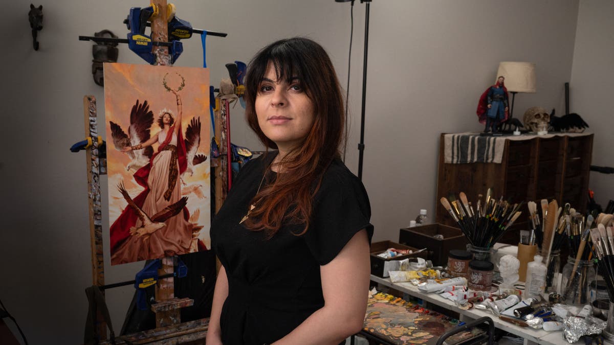Karla Ortiz posiert in ihrem Kunstatelier mit einem Gemälde im Rücken