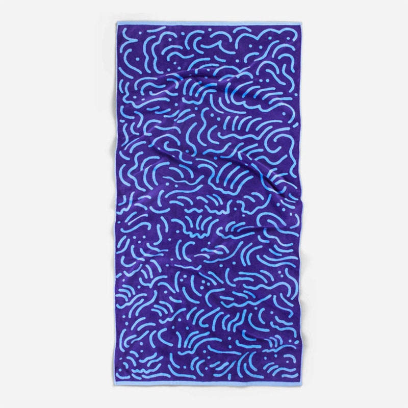 Strandtuch der Brooklinen Artist Series: Ein dunkelblaues Strandtuch mit einem hellblauen Kringelmuster auf grauem Hintergrund