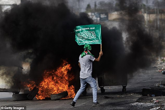 Witnesses said the Israeli forces unleashed artillery and tank fire on Gaza as well as the 'unprecedented' airstrikes. Pictured: A youth waves a Hamas flag in the West Bank