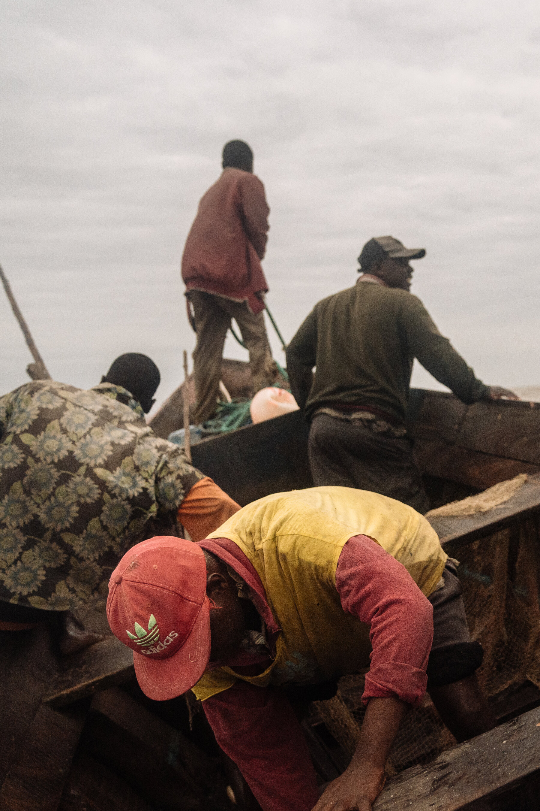 Five fishermen working in a wooden boat on a gray sea under gray skies.