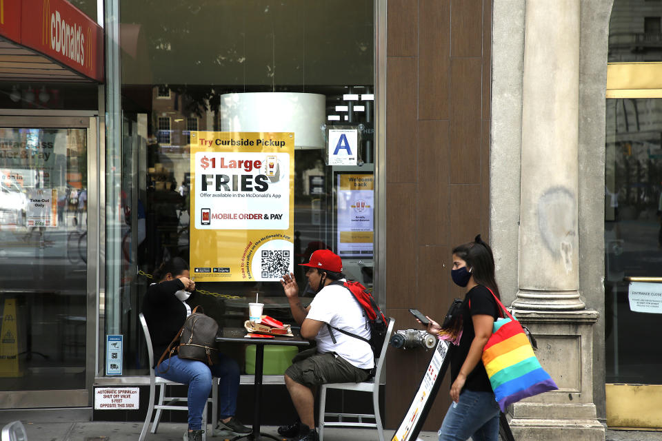 NEW YORK, NEW YORK – 17. AUGUST: Eine Frau mit Schutzmaske geht an einem Paar vorbei, das bei McDonalds isst.  (Foto von John Lamparski/Getty Images)