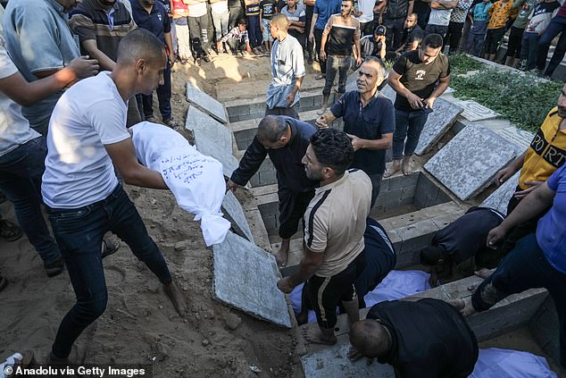 People help burying the shrouded bodies during the funeral of the members of Al-Ahcazi family, who lost their lives after Israeli airstrikes on their building in Rafah, Gaza, on Tuesday