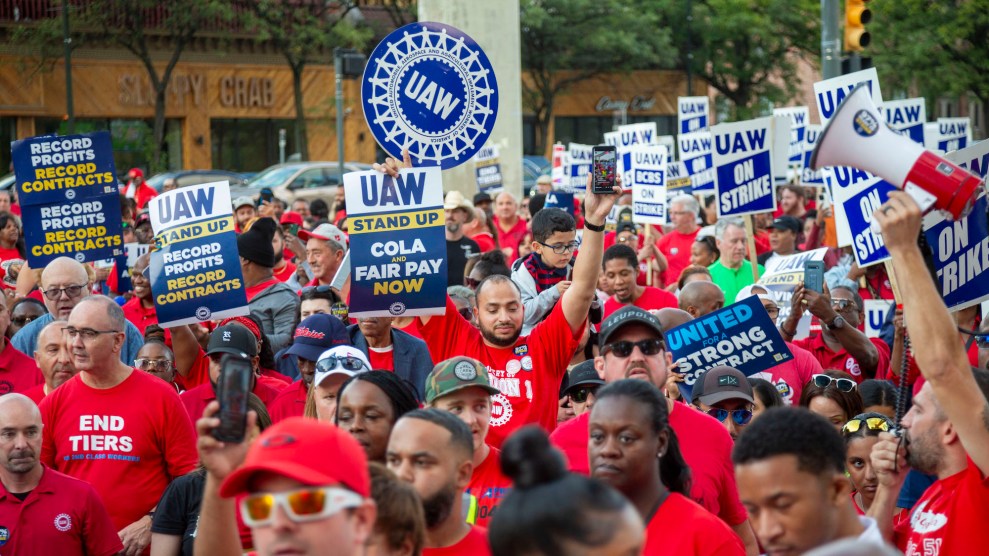 Streikende UAW-Mitglieder in roten Hemden halten Schilder mit der Aufschrift „ "UAW," "UAW: COLA Fair Pay Now" Und "UAW im Streik"