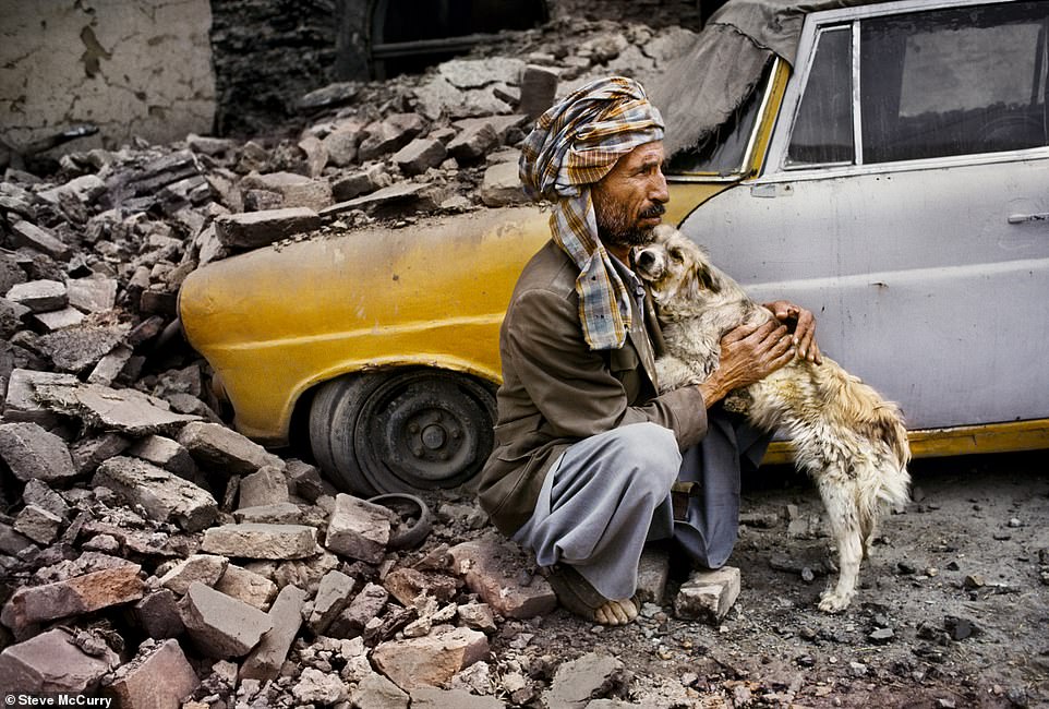 In Kabul, Afghanistan, sieht man einen Mann, der seinen Hund umarmt, neben seinem Taxi, das zerstört wurde, als das nahegelegene Gebäude durch Beschuss einstürzte.  Das emotionale Foto wurde 1992 von McCurry aufgenommen