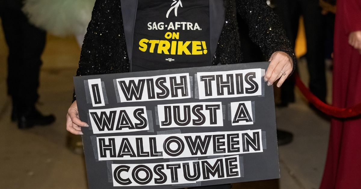 SAG-AFTRA-Mitglied trägt eine "SAG-AFTRA im Streik" Hemd, während er ein Schild hochhält, auf dem steht: "Ich wünschte, das wäre nur ein Halloween-Kostüm."