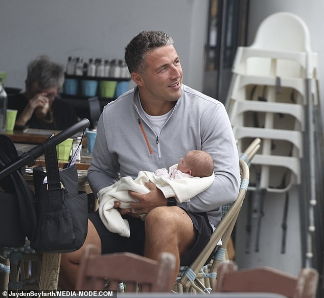 Das Neugeborene schien einigermaßen beruhigt zu sein, als Sam es hielt, während eine anbetende Lucy von einem Stuhl aus zusah