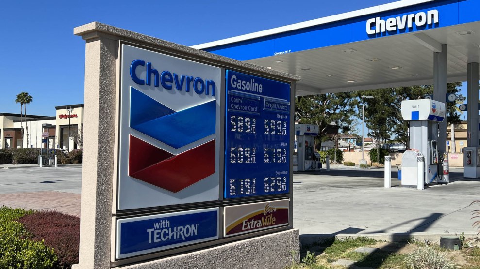 Ein Schild auf einem Chevron-Markt, auf dem die teuren Benzinpreise zu sehen sind, und auf dem Dach eines Gebäudes ist auch „Chevron“ zu sehen
