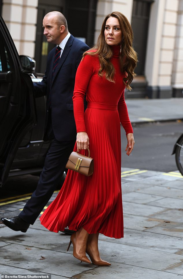 Kate Middleton sieht in einem roten Faltenrock und einem passenden Rollkragenpullover, gepaart mit hellbraunen Accessoires, stilvoll und raffiniert aus