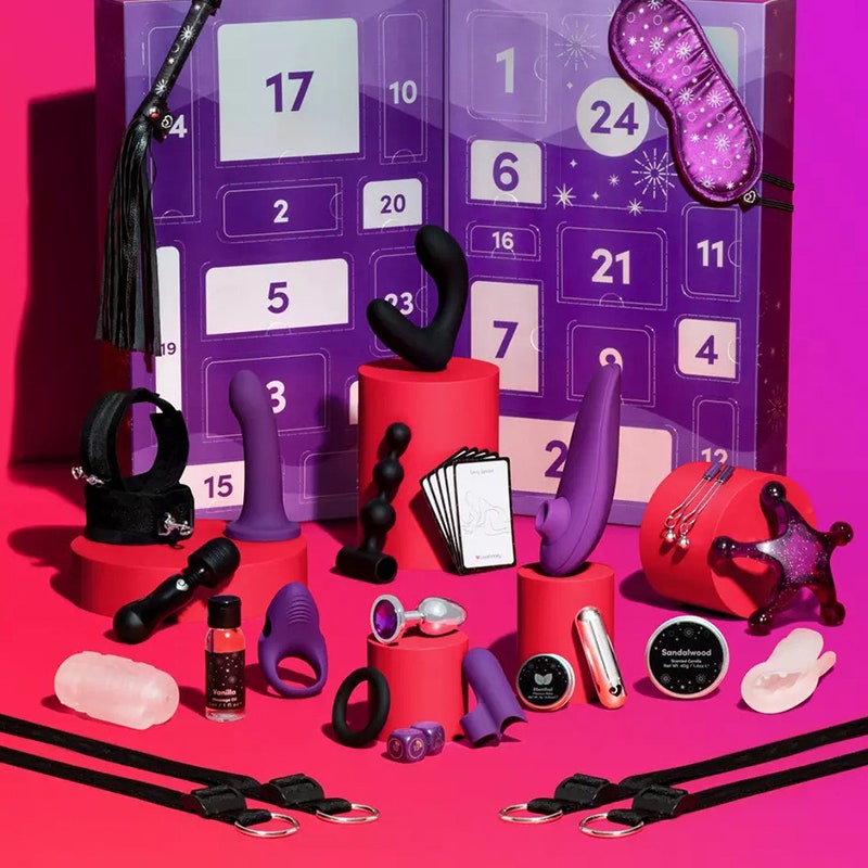 Lovehoney X Womanizer Sexspielzeug-Adventskalender: Eine Auswahl an Sexspielzeugen von Womanizer und Lovehoney vor einer lila Adventskalender-Geschenkbox auf rosa Hintergrund