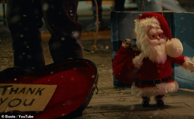 In der Anzeige entdeckt das junge Mädchen jemanden, der neben einer Miniaturausgabe des Weihnachtsmanns auf dem schneebedeckten Bürgersteig Straßenmusik macht