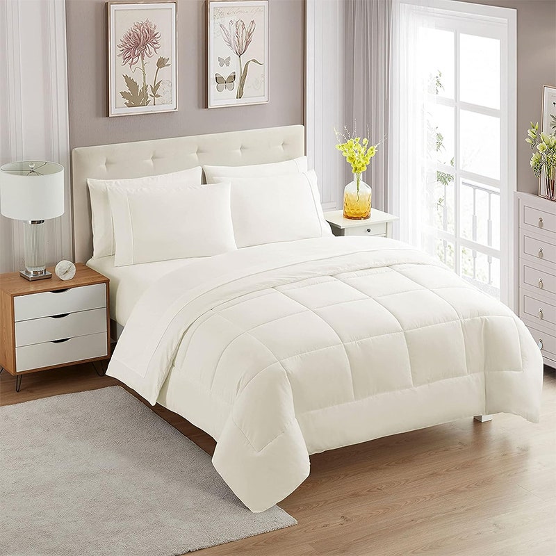 Bettdeckenset der Sweet Home Collection: Ein Bett mit weißen Laken in einem Zimmer mit Holzböden, einem großen weißen Fenster und grauen Wänden