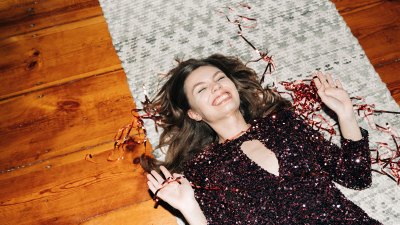 Fröhliche junge Frau im glitzernden Cocktailkleid auf Teppichboden, Blitzlicht, benutzergenerierte Inhalte